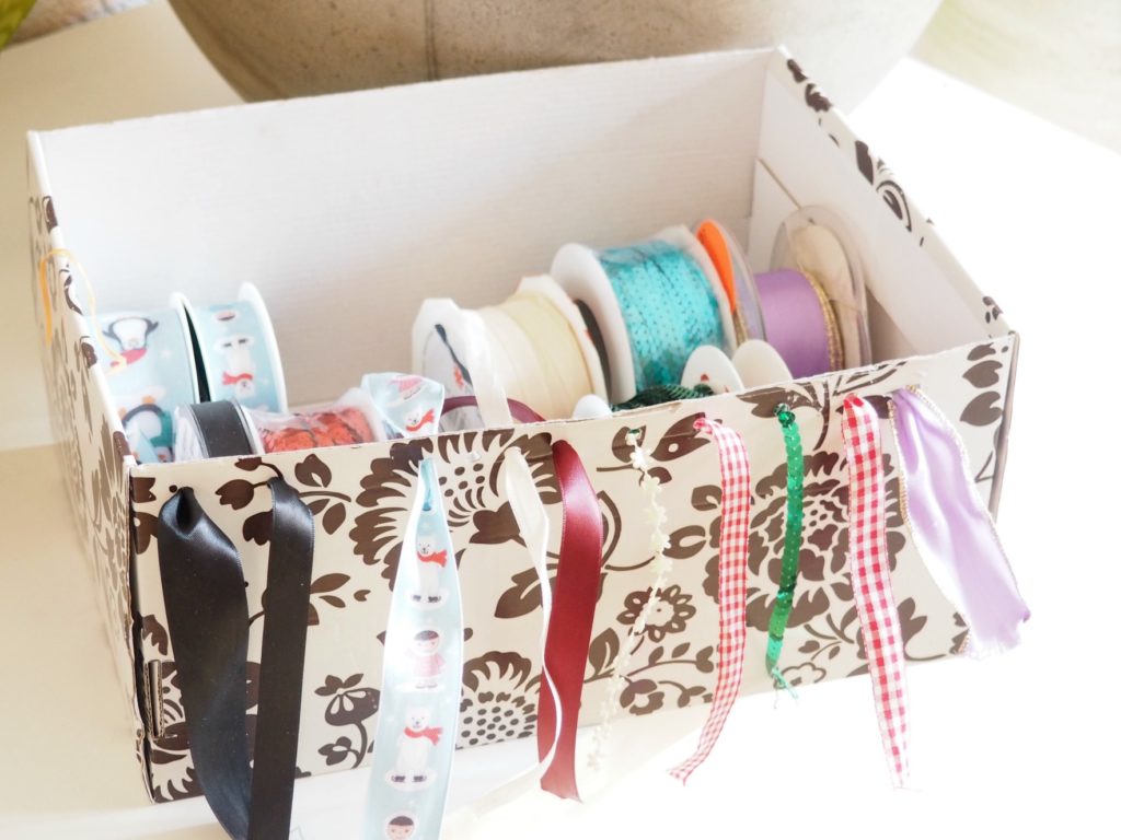 sortierte und entwirrte Dekobänder in einer Box mit Löchern am Rand, durch die die Borten gefädelt werden