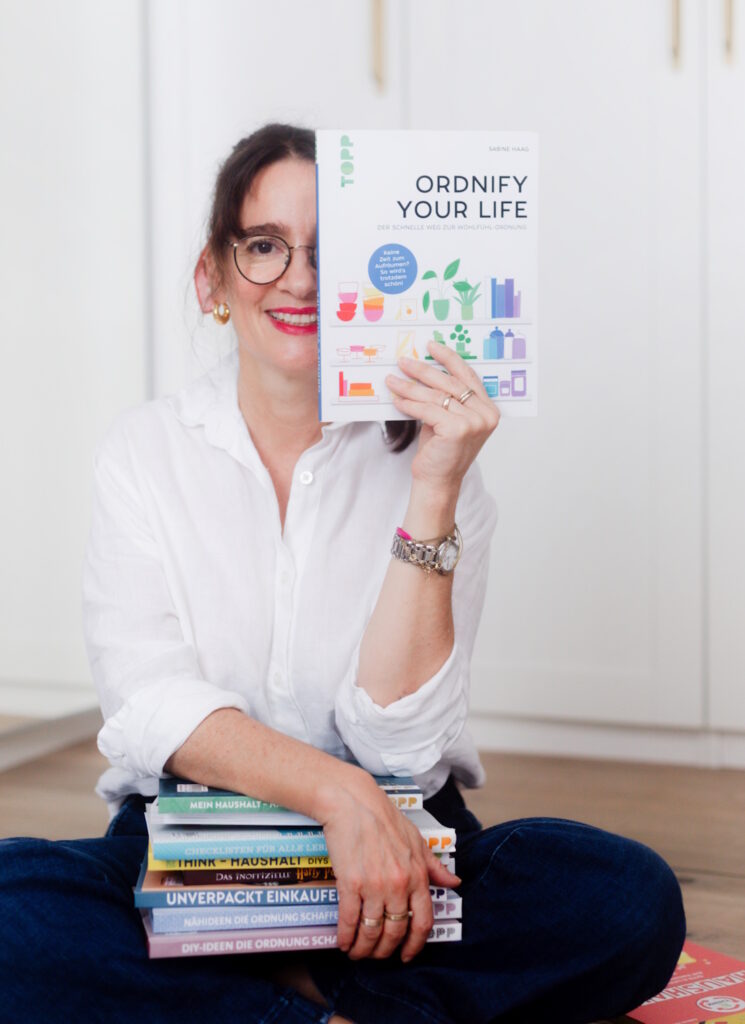 Die Autorin Sabine Haag hat einige ihrer Bücher auf dem Schoß und hält ihren Bestseller "Ordnify your life" in die Kamera.