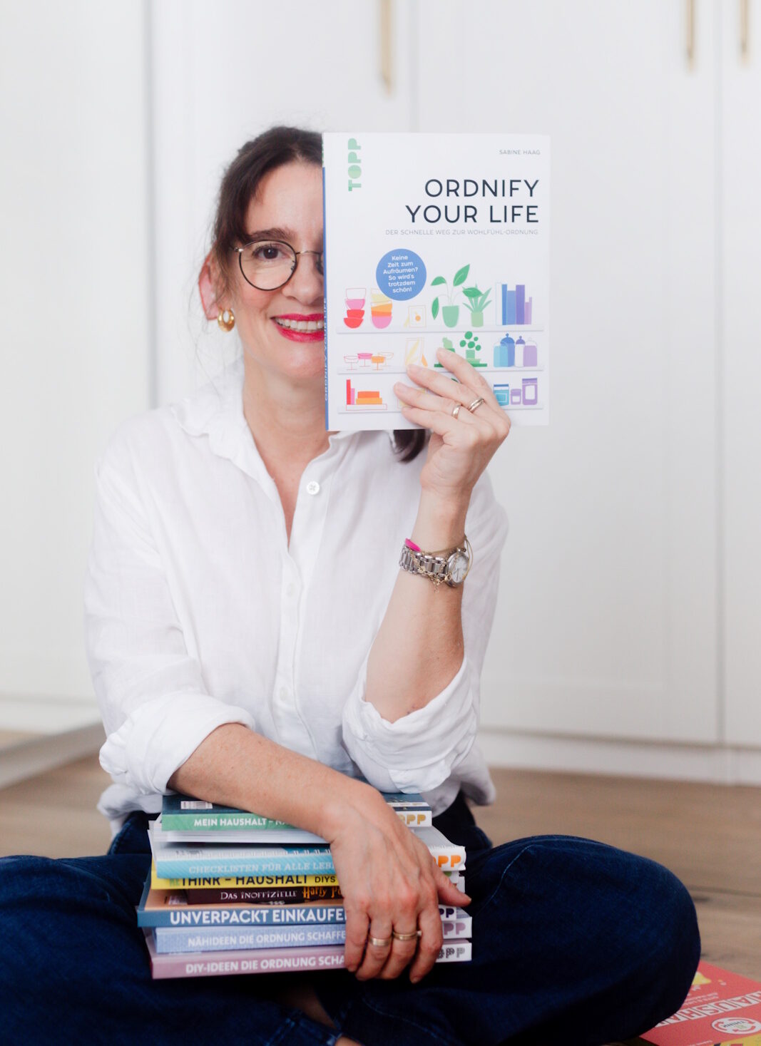 Die Autorin Sabine Haag hat einige ihrer Bücher auf dem Schoß und hält ihren Bestseller "Ordnify your life" in die Kamera.